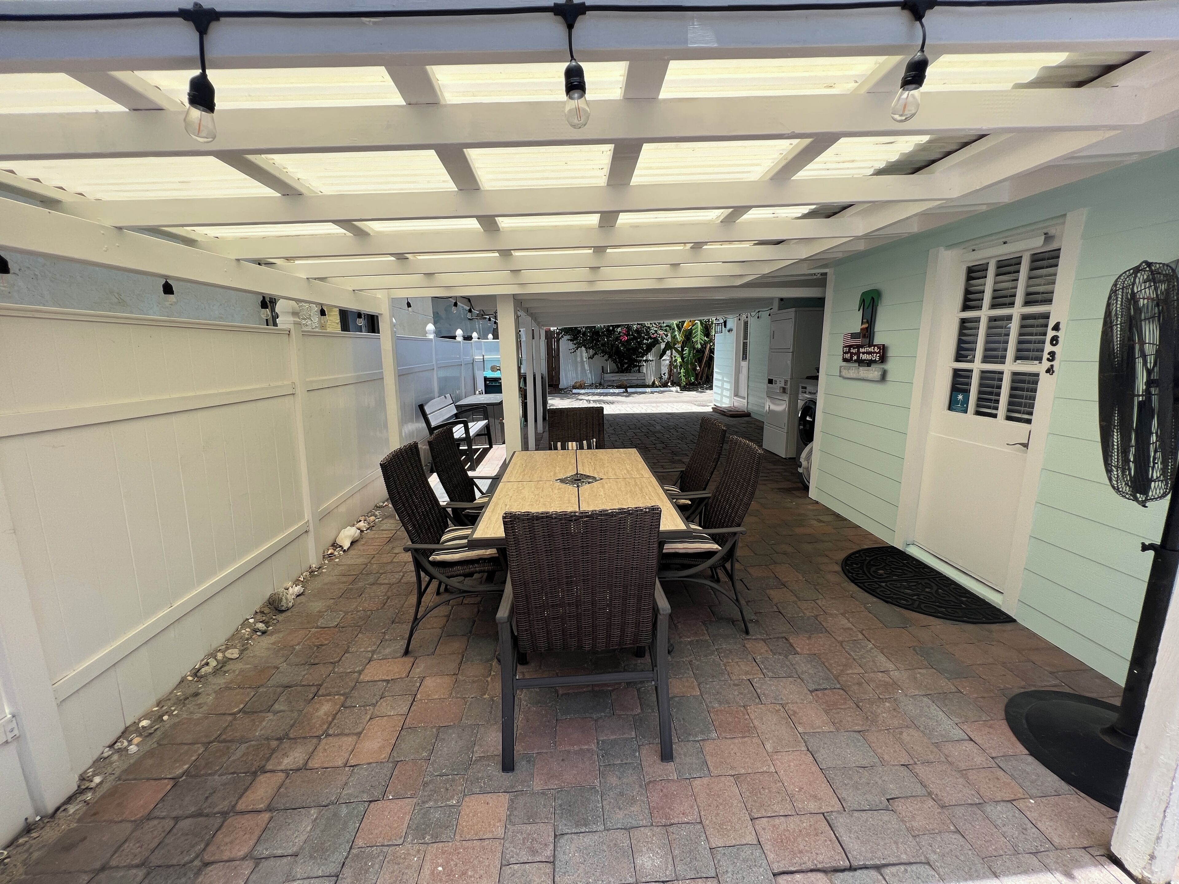 Un patio techado con una mesa y sillas, una valla blanca y una puerta con un número.