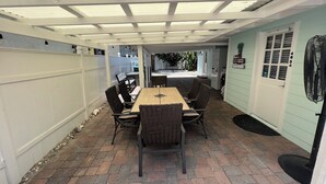 A covered patio with a table and chairs, a white fence, and a door with a number.