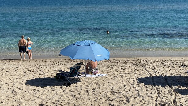 A beach with clear blue water, a sandy shore, and a blue umbrella providing shade.