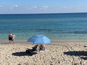 Une plage avec une eau d’un bleu limpide, un rivage sablonneux et un parasol bleu offrant de l’ombre.