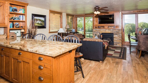 A spacious kitchen with wooden cabinets and a large island, a cozy living area with a fireplace, and a patio with outdoor seating. - Spacious Park City 4BR, Walk to Three Kings Lift, Mountain Views, Pool  & Hot Tu (Park City)
