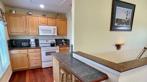 Une cuisine compacte avec des meubles en bois, un micro-ondes blanc, une cuisinière et un tabouret de bar.