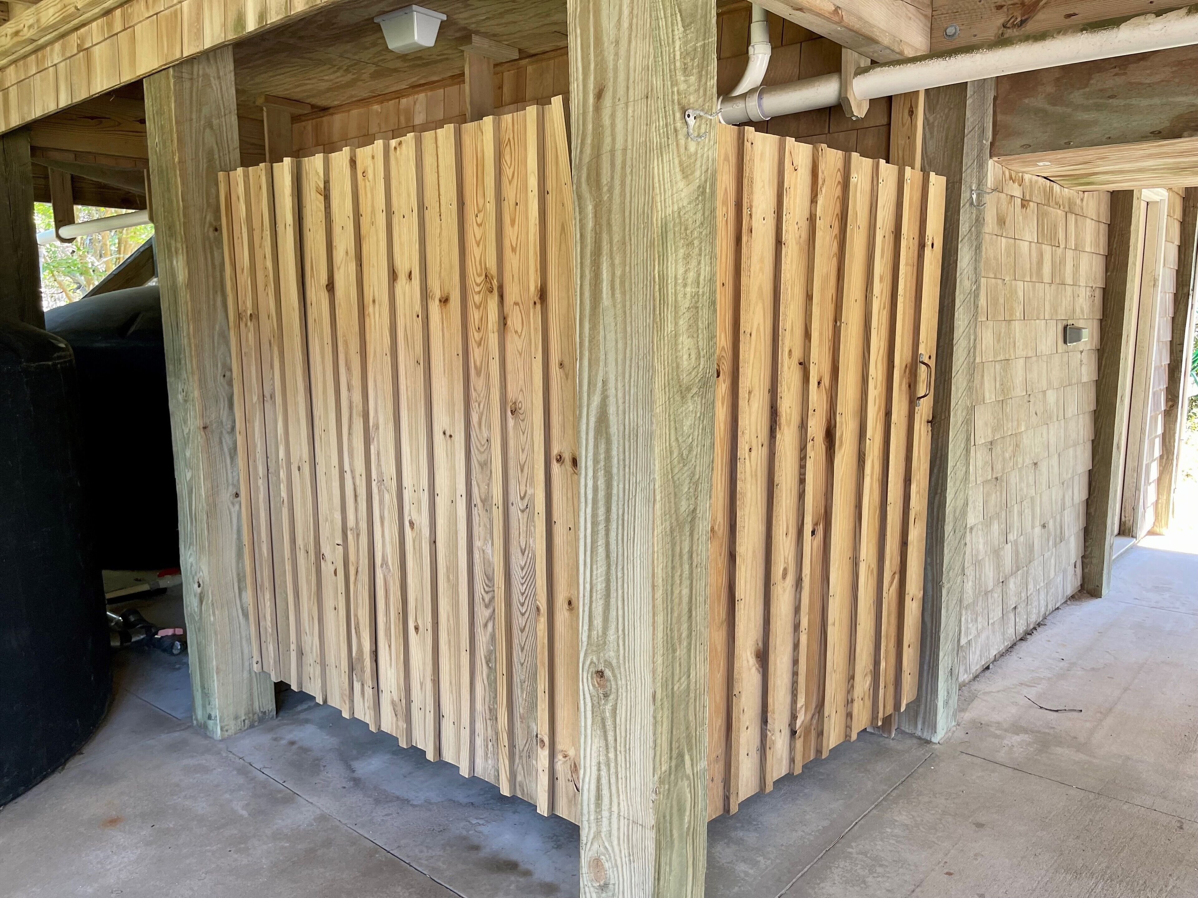 Una estructura de madera con tablones verticales, suelo de concreto y tuberías de fontanería a la vista.