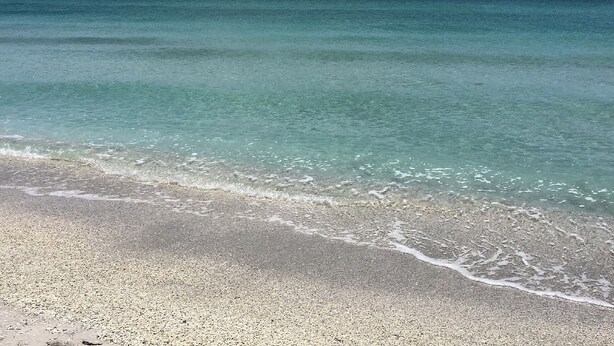 A beach with clear turquoise water and a pebbly shore.