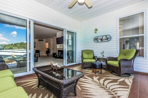 Un patio techado con muebles de mimbre, una mesa de centro de vidrio y vistas al exterior.