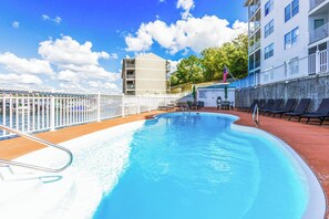 Un área de piscina con cerca blanca, sillas de descanso y un edificio con balcones.