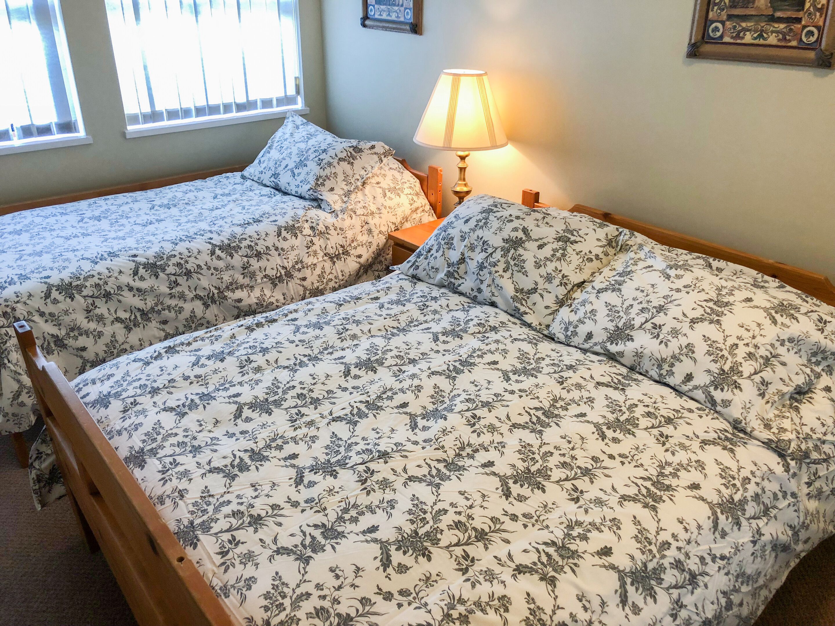 Two twin beds with floral bedding, a bedside lamp, and a window with blinds.