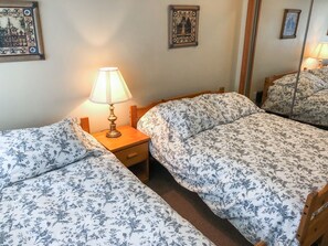 A bedroom with two single beds, a bedside table with a lamp, and a mirror on the wall. - Stoney Creek Northstar 36 (Whistler)