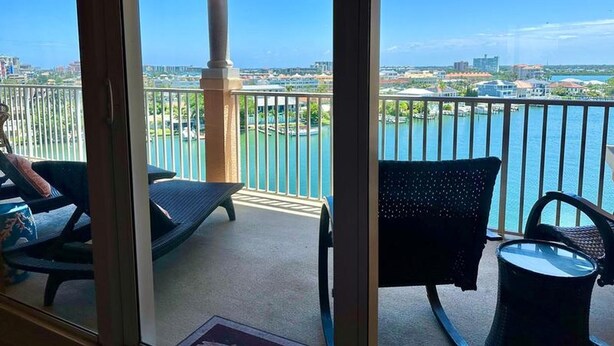 Un balcon offrant une vue sur une rivière et le paysage urbain, avec une chaise, une petite table et une rambarde.
