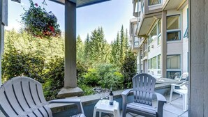 A balcony with outdoor seating, a hanging flower basket, and a view of a forested area.