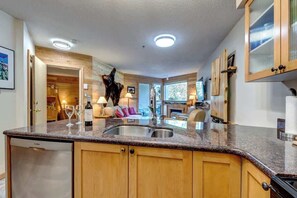 A kitchen with wooden cabinets, a granite countertop, and a dishwasher. - Greystone Lodge 229 Ski-in/Out by Acer Vacations (Whistler)