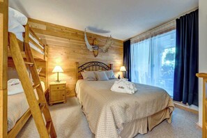 Una camera in stile baita con un letto a castello, un teschio di animale appeso al muro, un letto con coperta a motivi decorativi, lampade sui comodini e un'ampia finestra con tende.