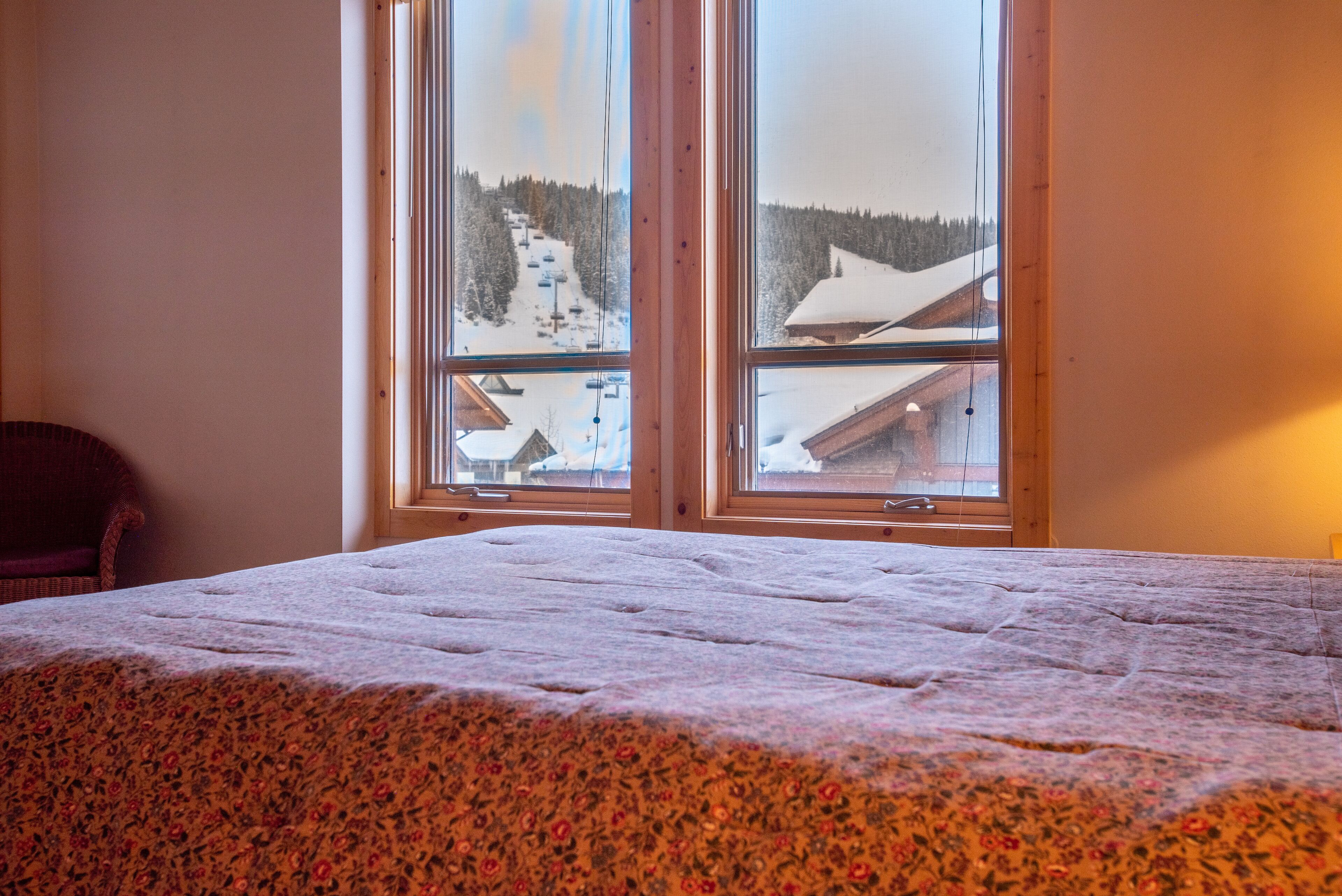 A room with a bed, a chair, and a large window with a view of a snowy landscape and buildings.