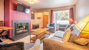 A cozy living room with a fireplace, a sofa, a coffee table, and a TV mounted on the wall. - Cozy Ski-in/Walk-out condo, free wifi, & parking, great value (Copper Mountain)