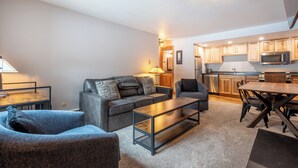 A modern living room with a sofa, armchair, and coffee table, a dining area with a table and chairs, and a kitchen with wooden cabinets and appliances. - Cozy Ski-in/Walk-out condo, free wifi, & parking, great value (Copper Mountain)