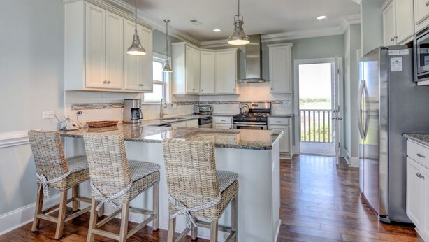 A spacious kitchen with white cabinets, a large island with bar stools, stainless steel appliances, and a view to the outdoors.