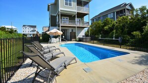 A swimming pool with lounge chairs and an umbrella, surrounded by a fence and buildings.