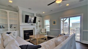 A living room with a fireplace, a television mounted above it, and a view of the beach through a large sliding glass door.