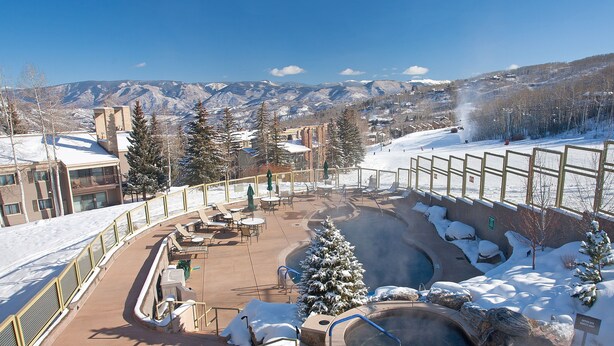 Un espacio exterior cubierto de nieve con un jacuzzi, asientos y vistas a montañas.