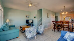 A living room with a sofa, a coffee table, a TV, and a dining area with chairs and a table. - Experience beachside bliss at Almost Heaven North, a spacious 4-bedroom duplex in North Topsail! (North Topsail Beach)