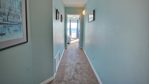 A hallway with light blue walls, carpeted floor, framed pictures, and a door leading to a balcony. - Experience beachside bliss at Almost Heaven North, a spacious 4-bedroom duplex in North Topsail! (North Topsail Beach)