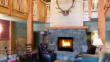 A spacious living room with a stone fireplace, wooden beams, and a chandelier.