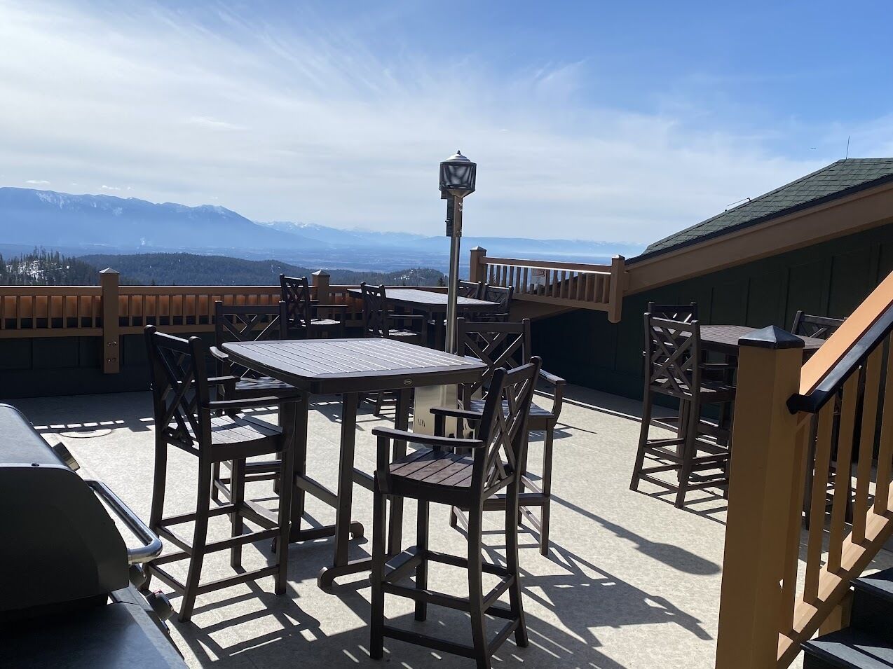 An outdoor patio with tables and chairs, a lamp post, and a view of mountains.