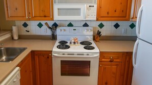 A kitchen with wooden cabinets, a white stove, a microwave, and a refrigerator. - Great Value Village Condo, Close to Everything, Hot Tub Access, Free Parking (Whistler)