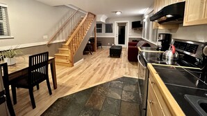 A modern kitchen with wooden cabinets, a black stove, and a dining area with a wooden table and chairs. - Cozy 2 Bedroom Waterfront Cottage with Hot Tub! (Ucluelet)