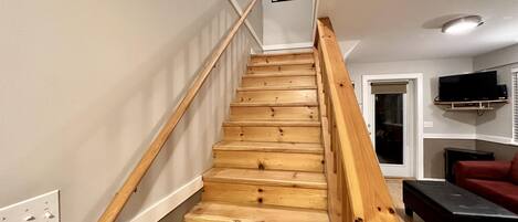 Un escalier en bois avec une rampe, un tableau encadré accroché au mur, un téléviseur fixé au mur et un canapé rouge dans le salon.