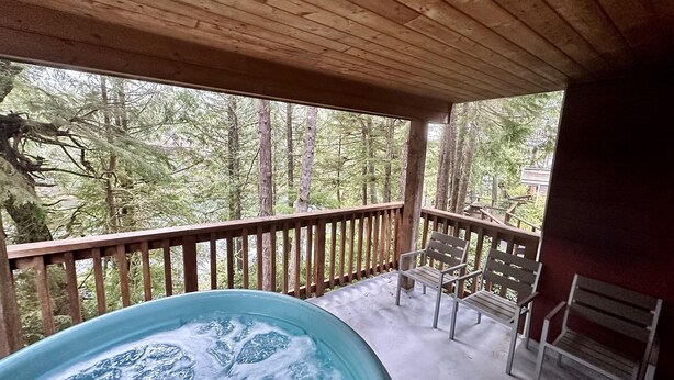 A wooden deck with a hot tub and two chairs, overlooking a forested area. - Cozy 2 Bedroom Waterfront Cottage with Hot Tub! (Ucluelet)