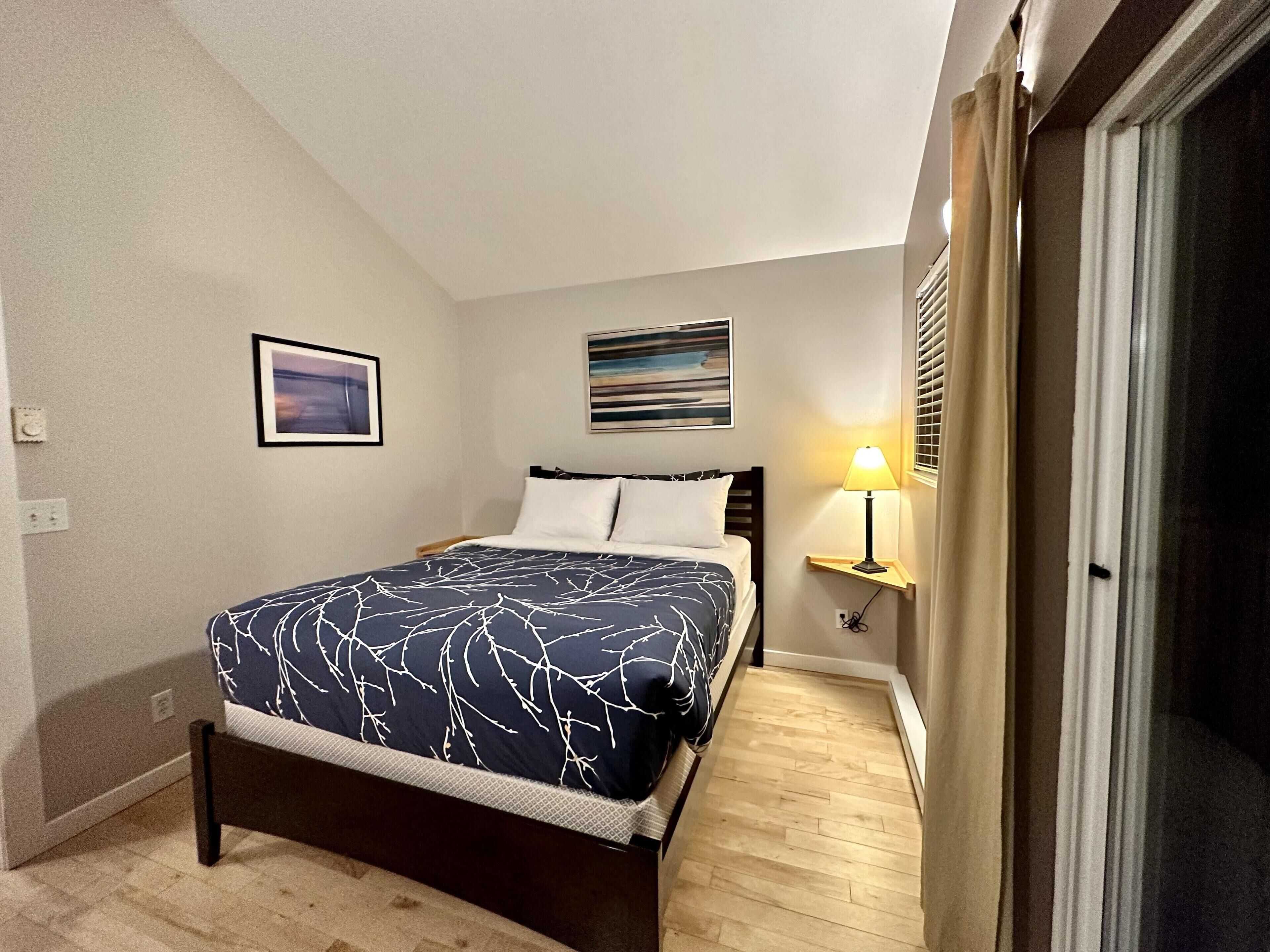 A bedroom with a bed, a nightstand, a lamp, and two wall art pieces.