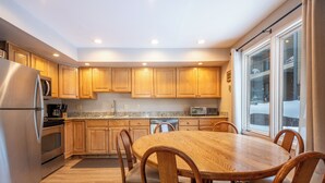 Una cocina moderna con armarios de madera, un refrigerador de acero inoxidable, una mesa de comedor con sillas y un ventanal grande.