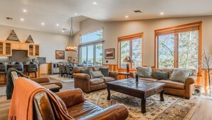 A spacious living area with leather sofas, a coffee table, and a dining area with a kitchen in the background. - Fantastic Mountain Townhome! Shared Hot Tub! Pool Table! Views! (Mammoth Lakes)
