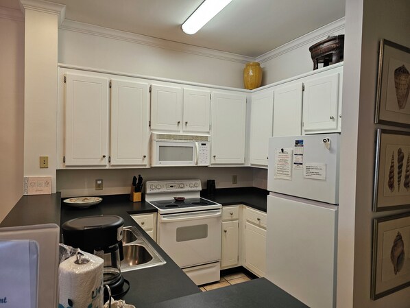 Una cocina con armarios blancos, microondas, estufa y refrigerador.