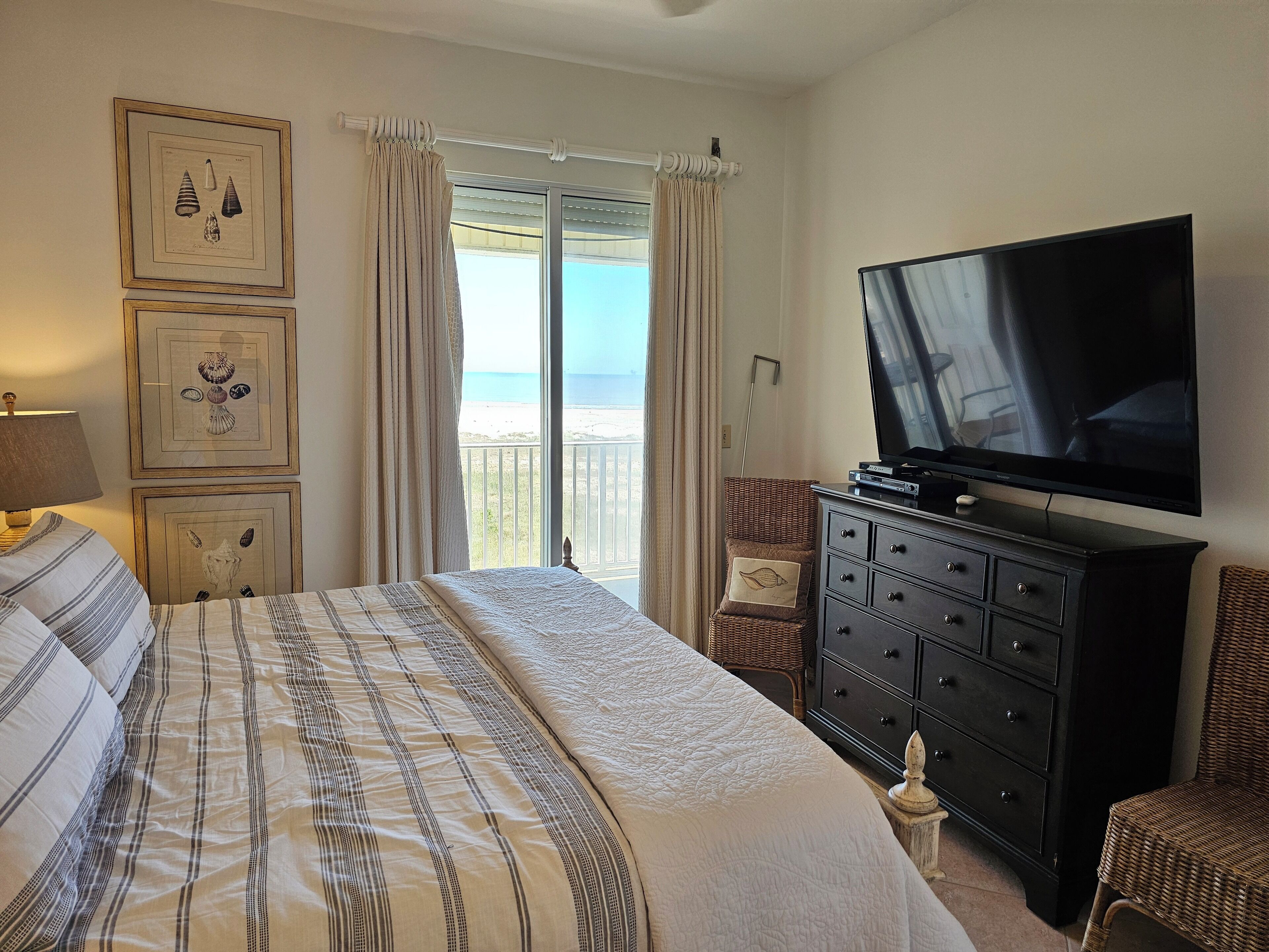 A bedroom with a bed, a dresser, a television, and a view of the ocean.