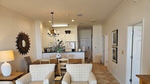 A living room with a dining area, a chandelier, and a kitchen in the background. - Inn at Dauphin Island 411 Beautiful Unit with Incredible Views!! (Dauphin Island)