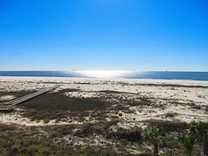 Une plage avec une promenade en bois qui mène à l’eau, des dunes de sable et un ciel bleu clair.