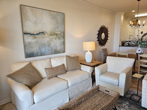 Un salon avec un canapé blanc, un fauteuil à motifs, une table basse et un tapis.