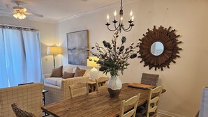 A dining area with a wooden table, wicker chairs, a vase with flowers, a chandelier, and a large mirror on the wall. - Inn at Dauphin Island 411 Beautiful Unit with Incredible Views!! (Dauphin Island)