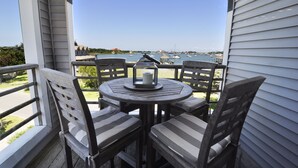 Ein Balkon mit rundem Tisch und vier Stühlen, Blick auf einen Yachthafen mit Booten und blauem Himmel.