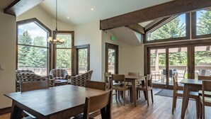 A spacious dining area with wooden tables and chairs, large windows with a view of trees, and a chandelier. - Snowcreek Condo 1516 - Room for up to 8 Guests & Sun Valley Resort Amenities (Sun Valley)
