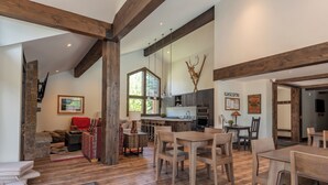 A spacious living area with a high ceiling, wooden beams, a stone staircase, a kitchen area, and a dining space with wooden furniture. - Snowcreek Condo 1516 - Room for up to 8 Guests & Sun Valley Resort Amenities (Sun Valley)