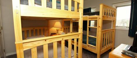 Una habitación con dos literas, una mesita de noche con lámpara y un televisor sobre un mueble de madera.