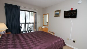 Habitación de hotel con una cama grande, un aparador, televisor montado en la pared y una ventana con cortinas.