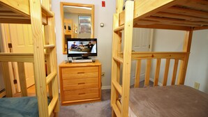 Habitación con literas, un aparador de madera y un televisor.
