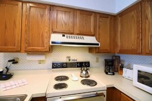 A kitchen with wooden cabinets, a stove, a microwave, and a kettle.