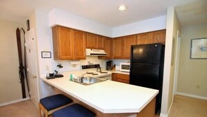 Una cocina compacta con armarios de madera, un refrigerador negro y una encimera blanca.