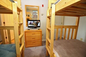 A bunk bed room with a television on a wooden dresser.