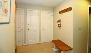 A hallway with two white doors, a fire extinguisher mounted on the wall, and a wooden bench.